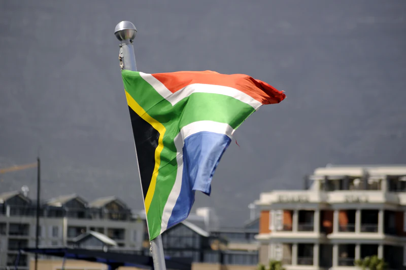The South African flag flying from a pole at the V&A Waterfront, with Table Mountain out of focus behind it.